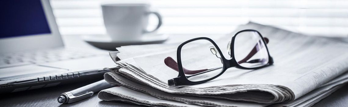 Brille liegt auf einer Zeitung, dahinter ist ein Laptop und Kaffee